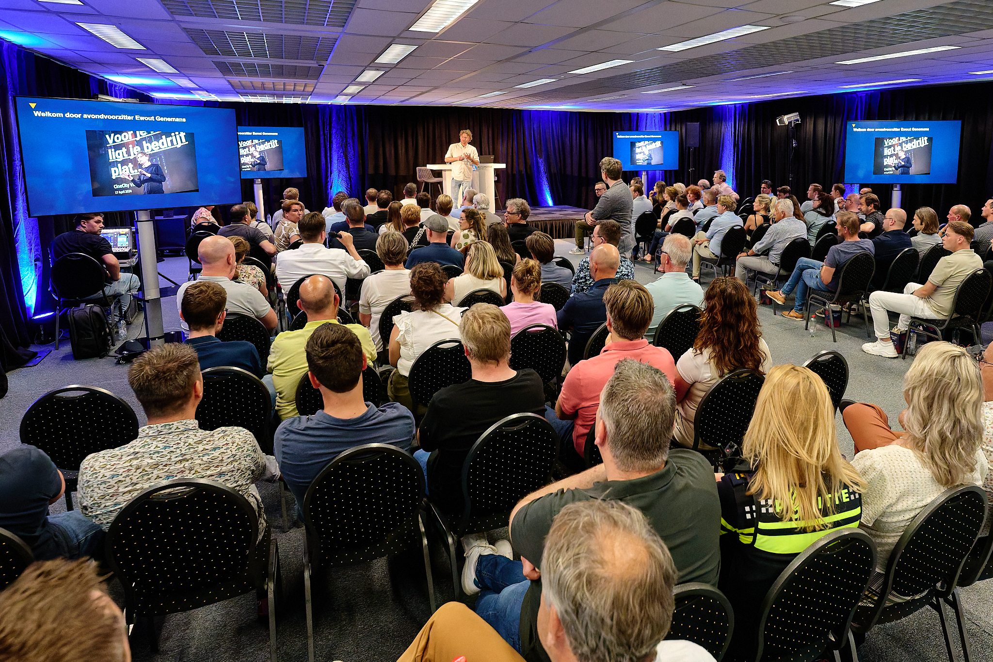Een bijeenkomst van PVO Zeeland West-Brabant waarbij de zaal vol zit met mensen en Ewout Genemans aan het spreken is op het podium.