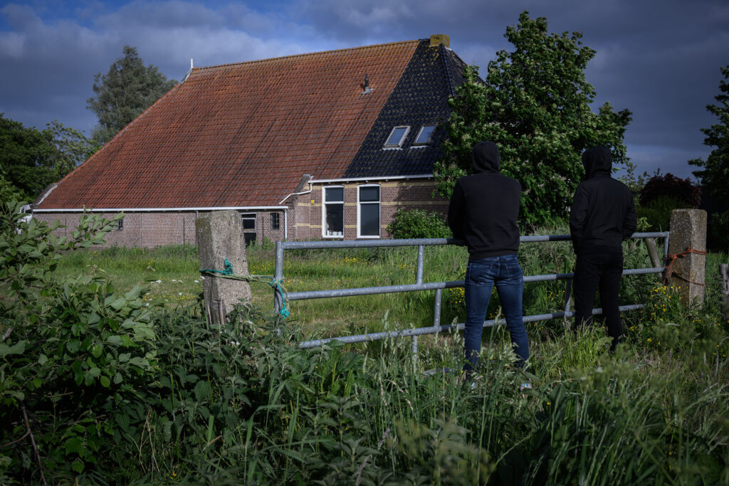 Twee personen met donkere kleding die naar een boerderij kijken. Beeld ter illustratie.